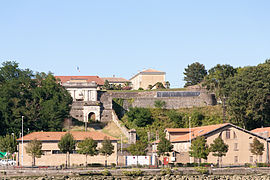 Vue de remparts surplombant deux bâtiments ocre.