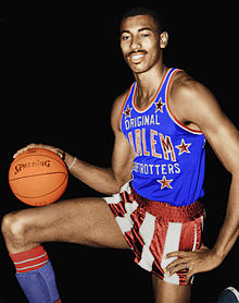 A basketball player, wearing a blue jersey with the word "ORIGINAL HARLEM GLOBETROTTERS" on the front, is posing while holding a basketball.