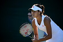 Une joueuse de tennis en tenue blanche regarde au loin raquette en mains.