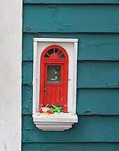 A photograph of a small, red door on the side of a building.