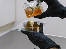 An artist wearing gloves pours liquid salt collodion onto a glass plate.