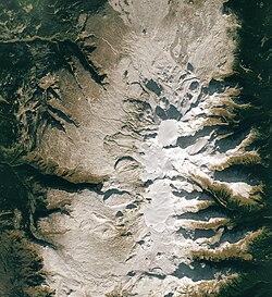 An overhead view of a barren, rocky plateau with a glaciated mountain in the middle.