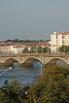 Vue de trois arches d’un pont orné de drapeaux, sur fond de bâtiments.