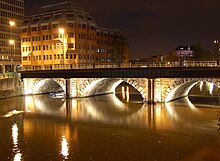 A three-arched bridge viewed from an oblique angle, illuminated by lights