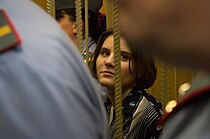 A woman with brown hair and a floral shirt. Her view is obstructed by two uniformed officers standing in front of her.