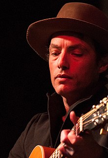 white male holding guitar while looking downwards