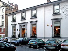 A two-storey white building with grey window frames, several cars parked in the foreground