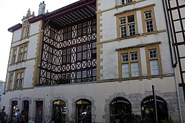 Vue d'un bâtiment à façade blanche à croisillons de bois rouge.