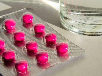 Unopened blister pack of pink pills next to a glass of water