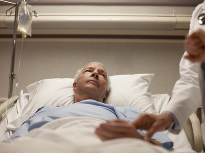 doctor taking pulse of senior man in hospital bed