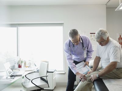 Doctor examining senior mans knee in examination room