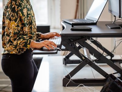 Cropped shot of a woman working at a standing desk in office. Female employee working at ergonomic standing desk.