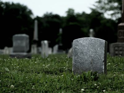 Tombstones On Grassy Field In Cemetery Against Sky