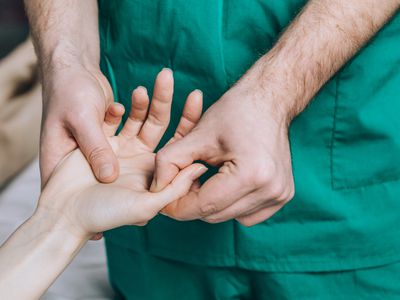 A male massage therapist puts pressure on a sensitive point on a woman's hand.