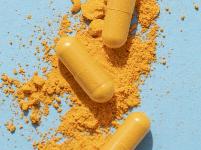 orange curcumin turmeric pills with powder and shadow on blue background