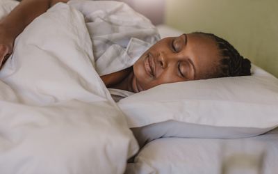 A Black woman sound asleep under a cozy duvet in her bed at home