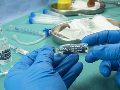 A close up of gloved hands holding a lidocaine vial