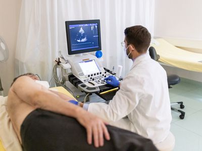 Doctor looking at the computer screen while doing an ultrasound test of a senior male patient lying on clinic bed