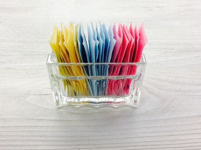 sugar substitute packets in a glass container on a white, painted wood surface - artificial sweetener - part of a series