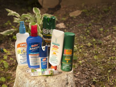 A collection of bug sprays and lotions are displayed on a tree stump