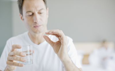 Man taking a white pill with a glass of water