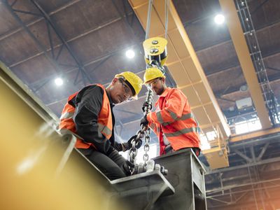 Steel workers fastening steel to crane in factory