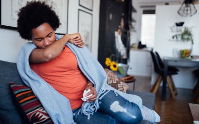 Person at home on sofa coughing, with tissue