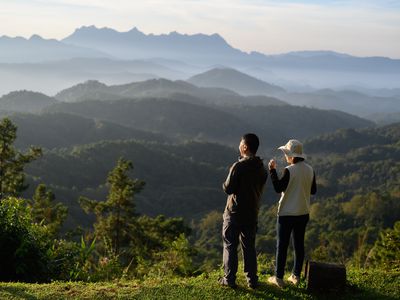 couple drinking coffee and admiring the mountainside scenery as the sun rises in the morning