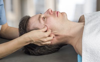 Physiotherapist, chiropractor doing a cranial sacral therapy to a man patient. Activating trigeminal nerve. Osteopathy.