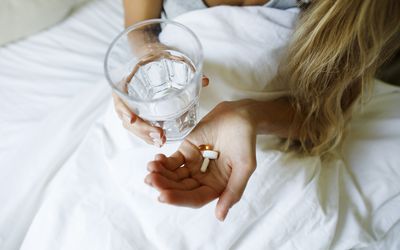 Woman taking supplements with glass of water in bed at home