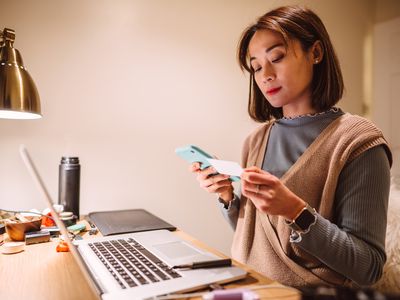 Woman in front of laptop checking her medical insurance card while holding phone