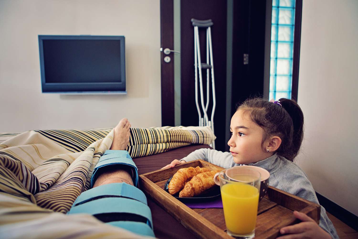 Man with injured leg in bed with girl bringing a breakfast tray