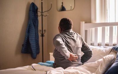 Person with hand on back in bed. Stock Photo