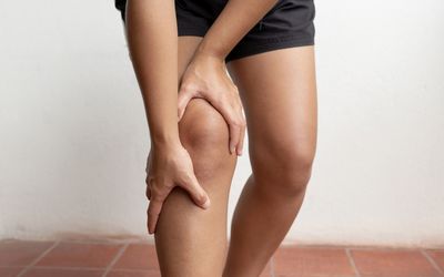 Person bending over holding their right knee and upper calf with both hands.