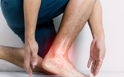 A person kneels, their foot in the foreground. Their foot has a digital illustration of an glowing red x-ray image, the bones of their foot showing, as though the foot is painful.