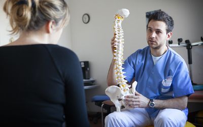 Young male doctor holding model spine in front of blonde woman with her back to the camera