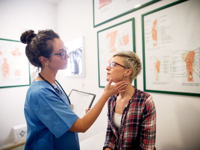 Doctor examining neck of young adult female patient 