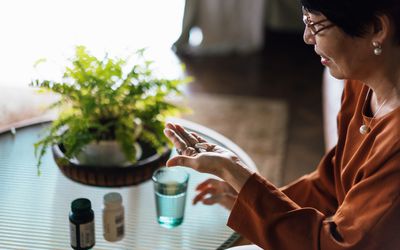 Older Asian woman taking medicines in hand with a glass of water at home.