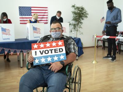 A man sitting in his wheelchair and holding a sign "I voted" on election day