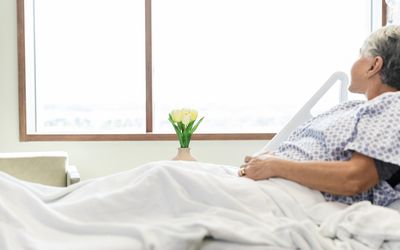 person laying in hospital bed looking out window