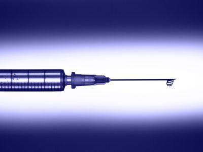 Disposable sterile syringe with drop of transparent medication on thin needle on violet background