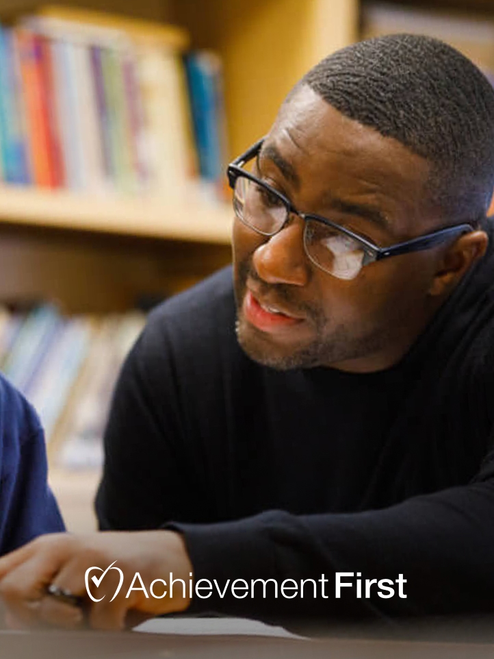 Achievement First team member working with a student, with the organization logo
