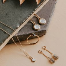 A variety of Hello Adorn gold jewelry on a terracotta background.