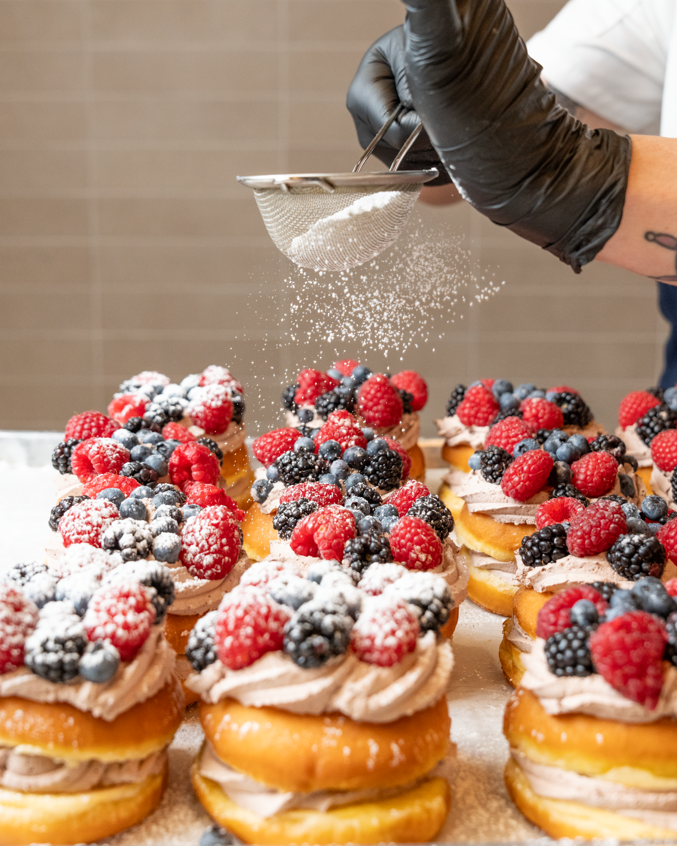 A row of berry-topped doughnuts gets a dusting of powdered sugar. 