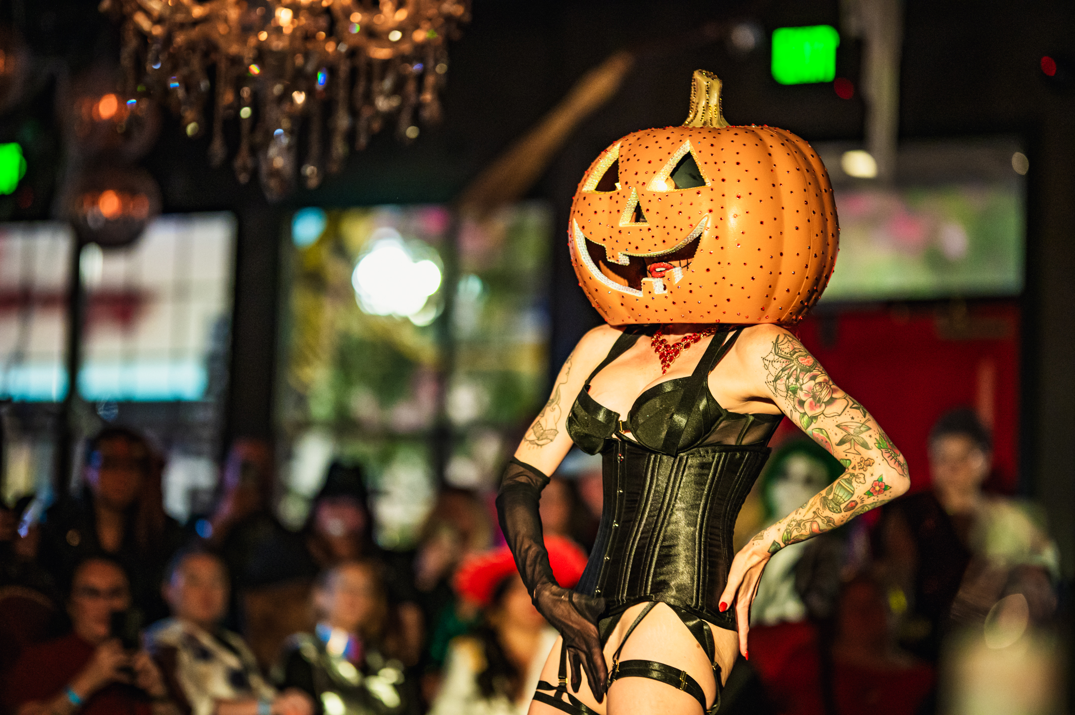 A burlesque dancer wearing a jack-o-lantern mask.