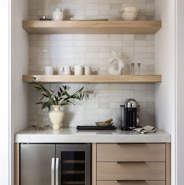 a compact kitchen nook features light wooden shelves mounted on a tiled wall, displaying various ceramic and decorative items