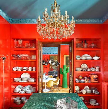 from the kitchen, a green marble countertop with built in shelves with dishware and glassware on either side of a door leading to a dining room with a large standing green cactus sculpture next to a table and chairs