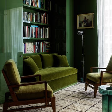 a study is done in shades of green the sofa and chair cushions are in a moss, lacquered cabinets are in a traditional green, a round side table is an emerald green, shelves behind sofa, light rug with black lines