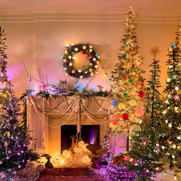 living room with many colorful, flocked, lighted christmas trees, a wreath over the fireplace, mantel decorations, and little globes inside the fireplace itself