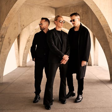 three individuals in formal attire standing under a concrete archway